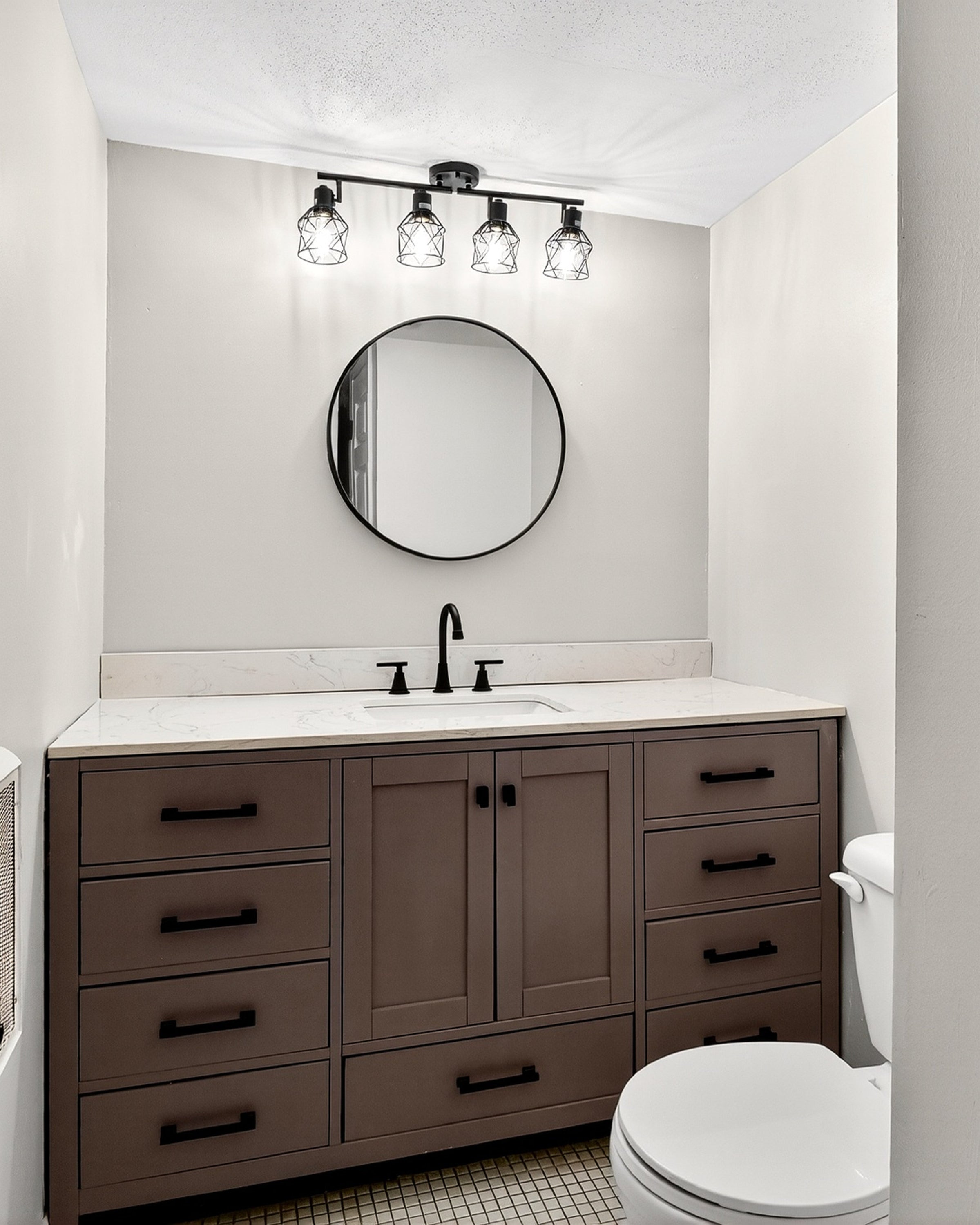 Bathroom with wooden vanity, round mirror, and toilet.