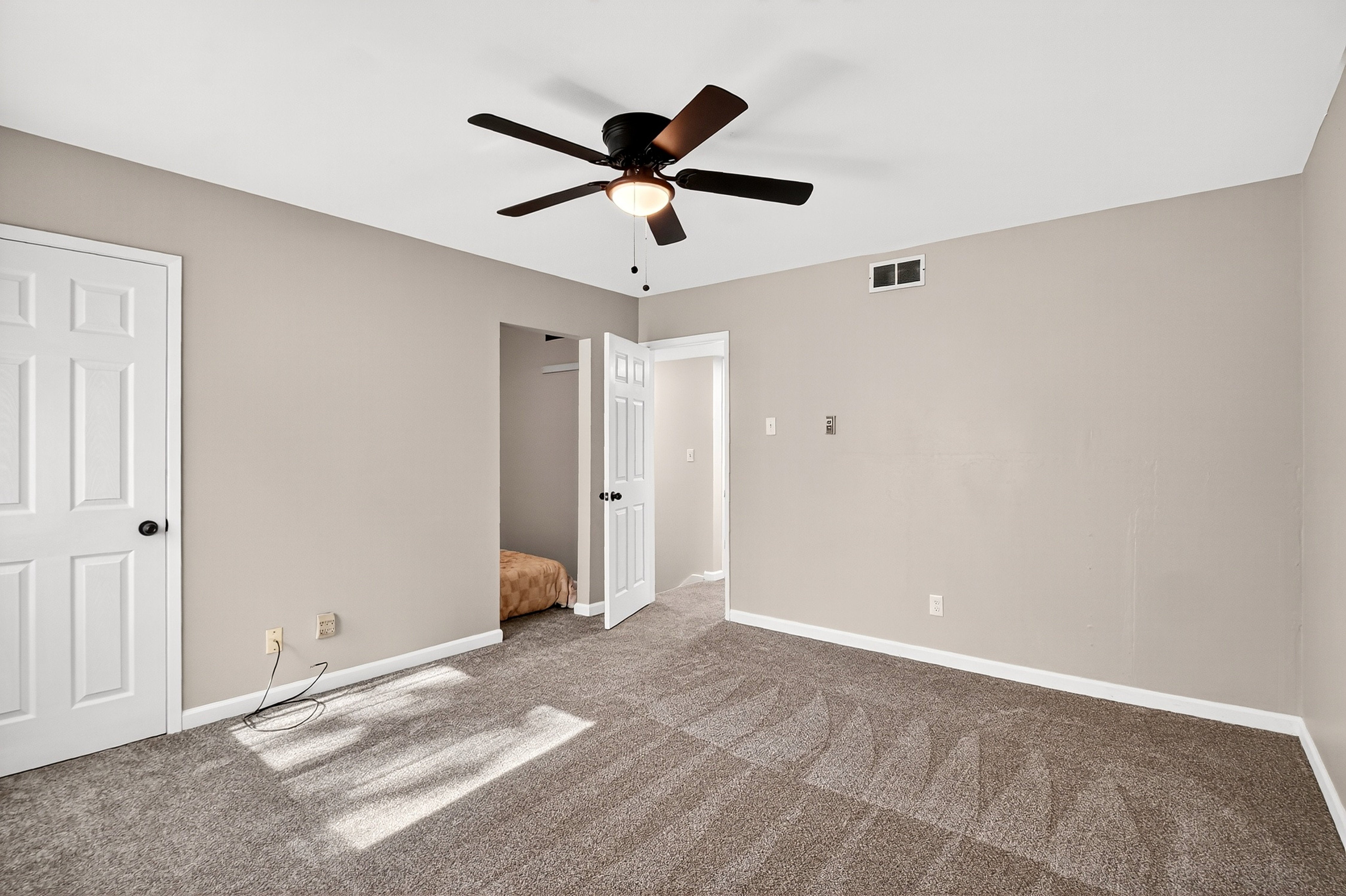 Empty room with beige walls, carpeted floor, and ceiling fan.