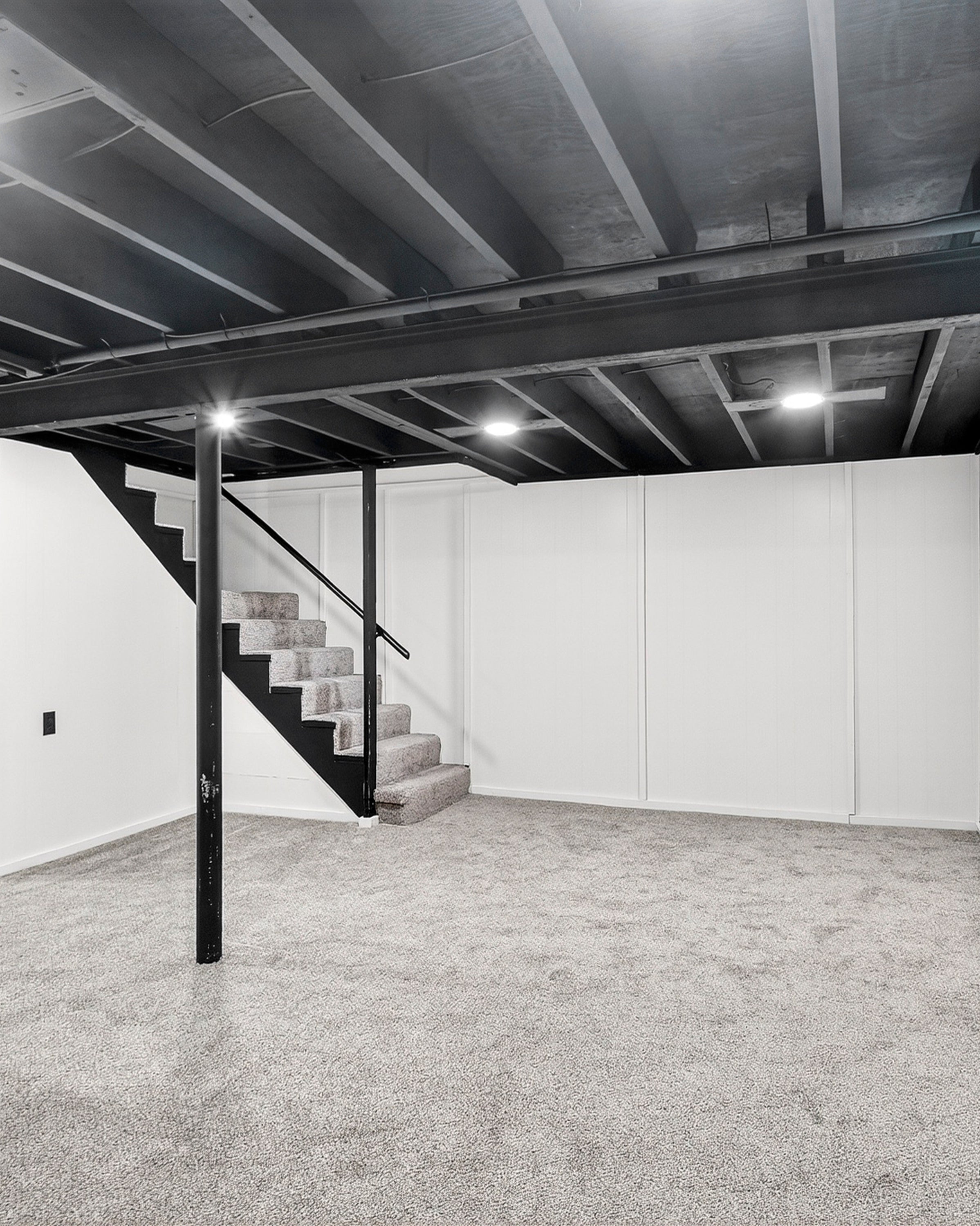 Basement with black ceiling beams, carpeted floor, and white walls.
