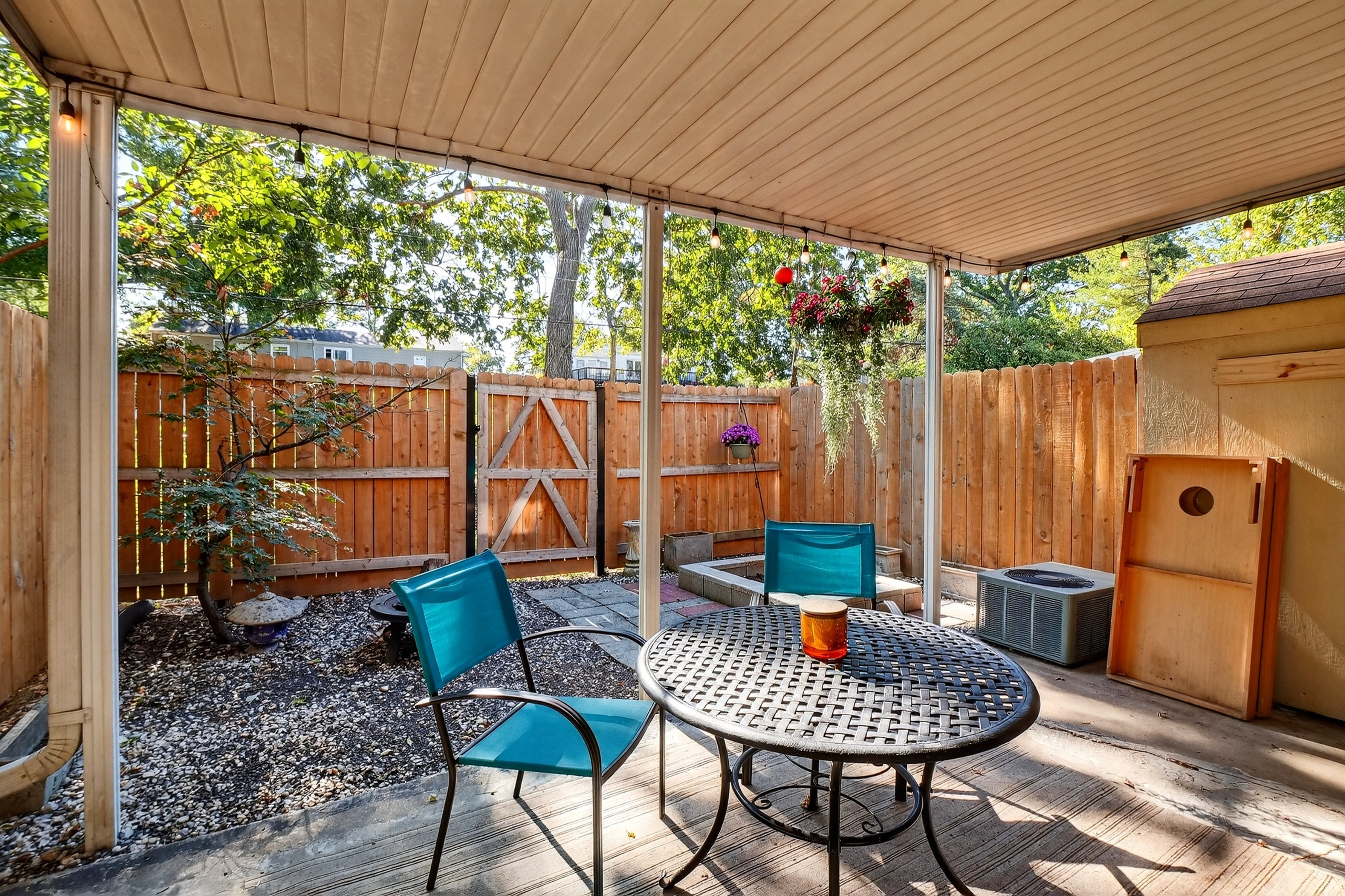 Outdoor patio with blue chairs and a table, surrounded by trees and wooden fence.