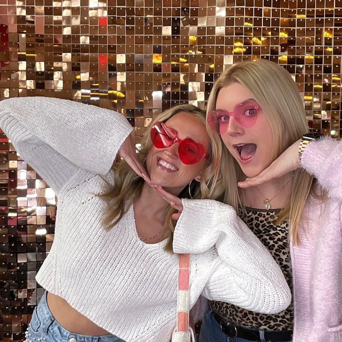 Two women posing in front of a glittery, multicolored background