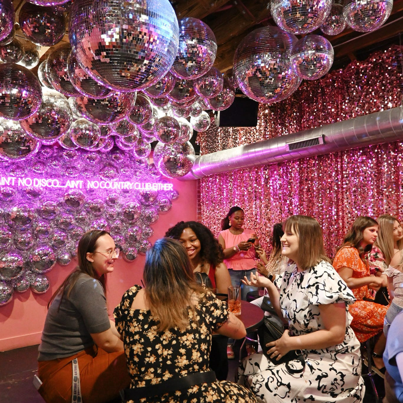 People socializing in a room with disco balls and pink walls