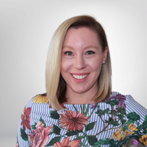 Woman with blonde hair wearing a floral-patterned shirt against a plain background