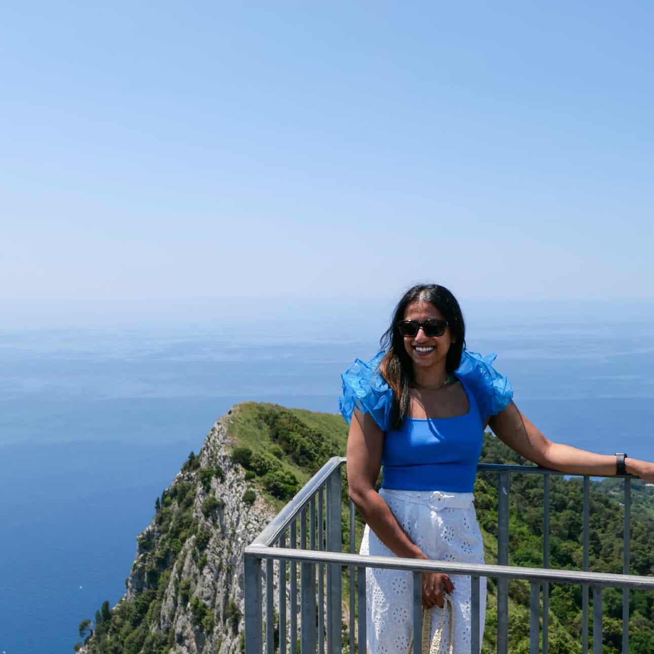 Woman in a blue dress standing on a cliff overlooking the ocean.
