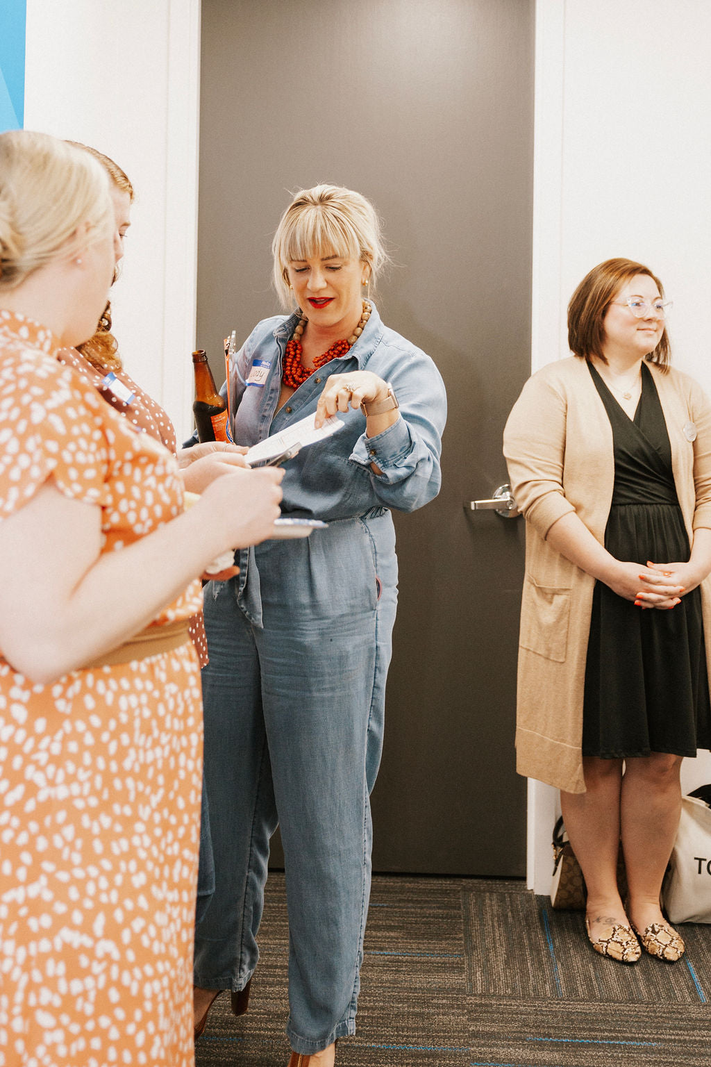 Three women standing in a room, with one handing something to another.