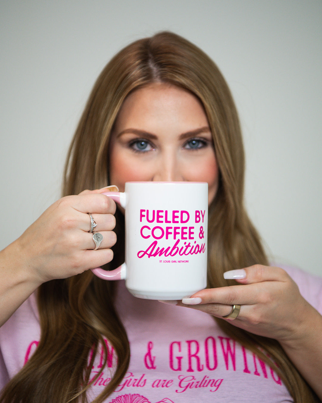 Woman holding a mug with 'Fueled by Coffee & Ambition' text, wearing a pink shirt.