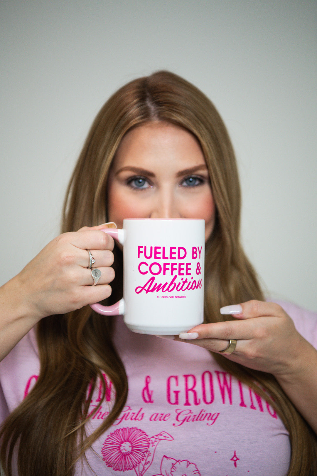 Woman holding a mug with 'Fueled by Coffee & Ambition' text, wearing a pink shirt.