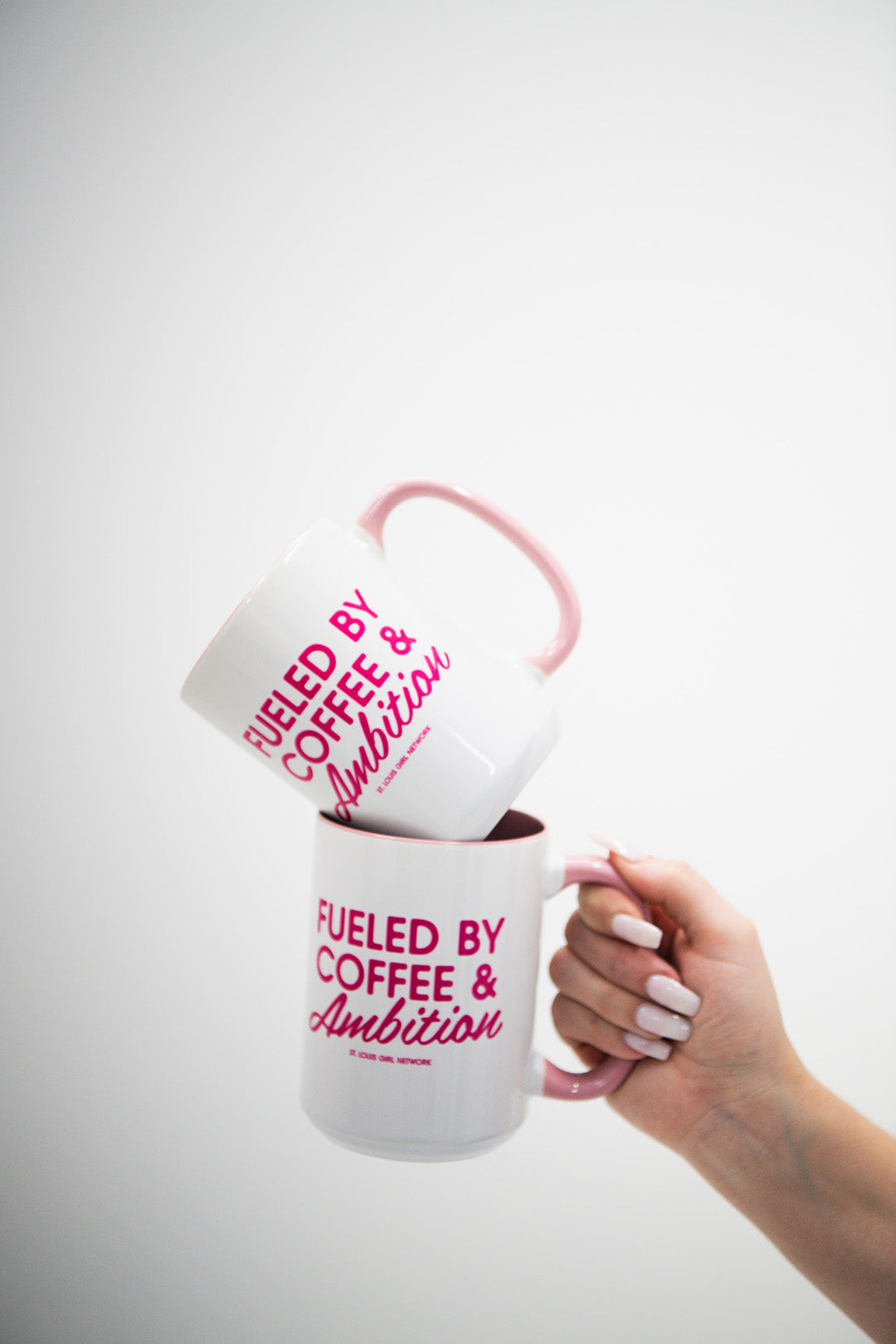Hand holding a white mug with pink text 'Fueled by Coffee & Ambition' against a white background