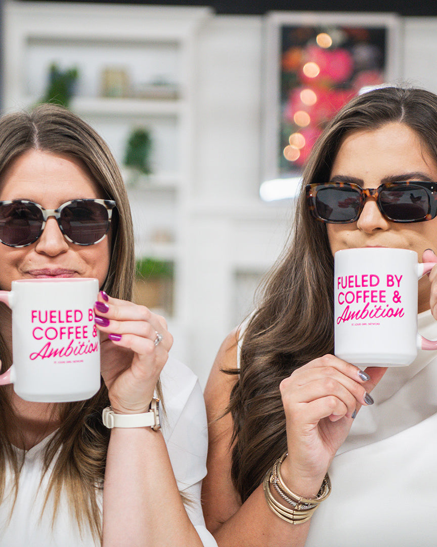 Two women holding mugs with 'Fueled by Coffee & Ambition' text in a casual setting.