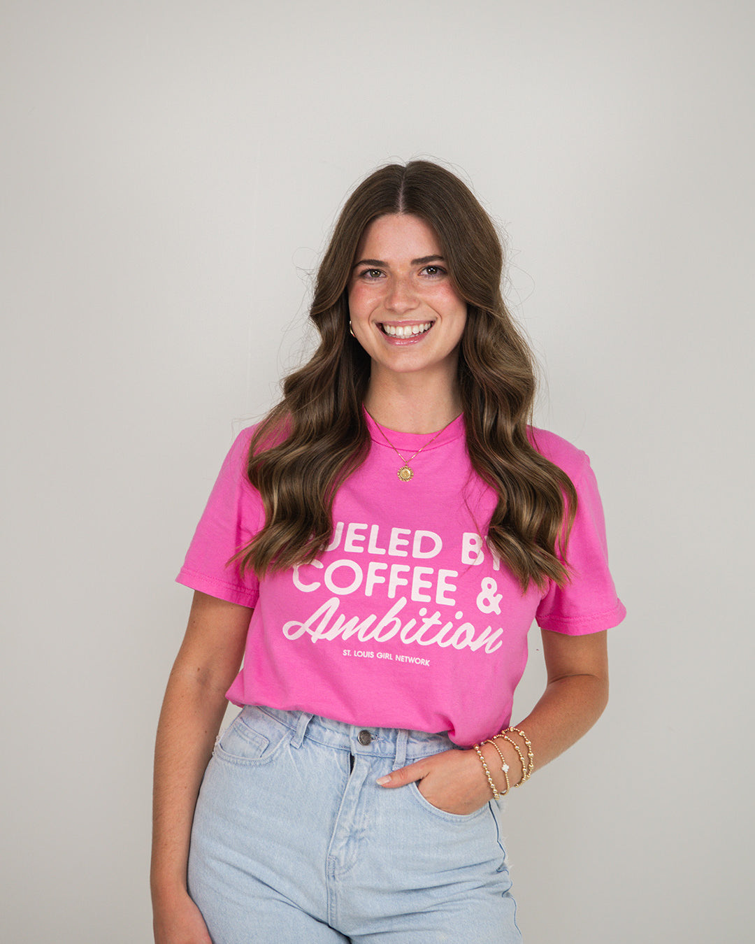 Woman wearing a pink t-shirt with text, standing against a plain background