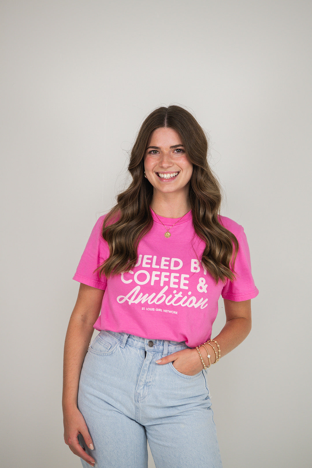 Woman wearing a pink t-shirt with text, standing against a plain background