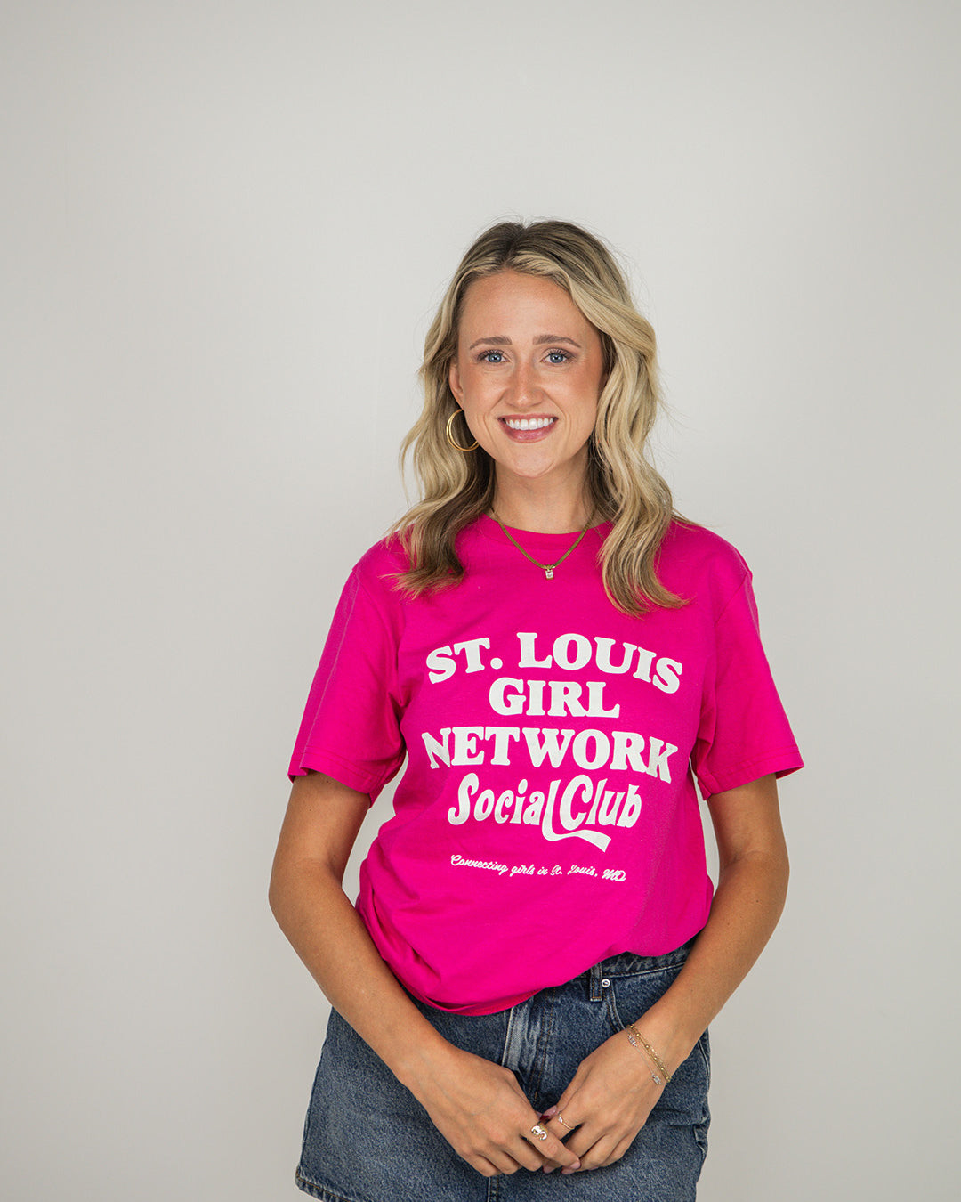Woman wearing a pink t-shirt with 'St. Louis Girl Network Social Club' text on a plain background