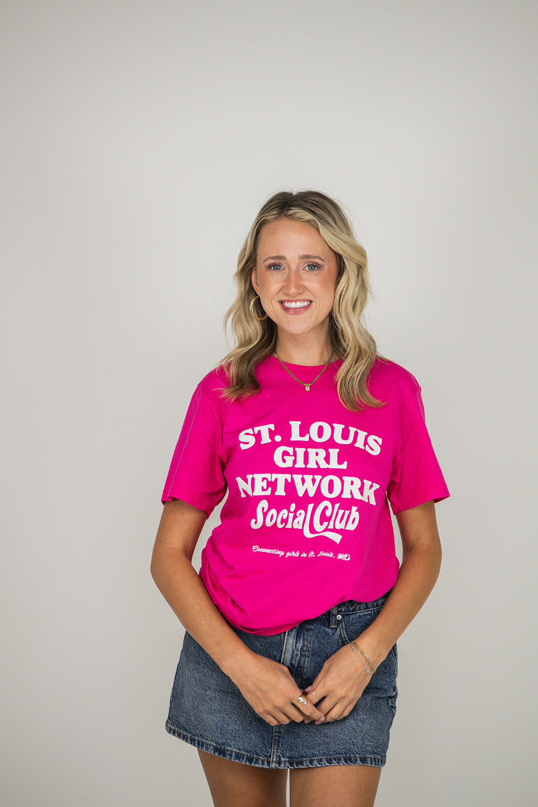 Woman wearing a pink t-shirt with 'St. Louis Girl Network Social Club' text on a plain background