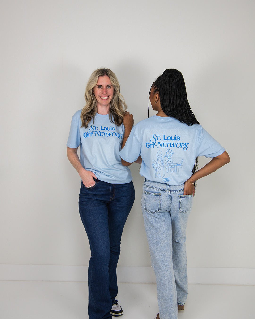 Two women wearing matching blue t-shirts with 'St. Louis Girl Network' text, standing side by side against a white background.