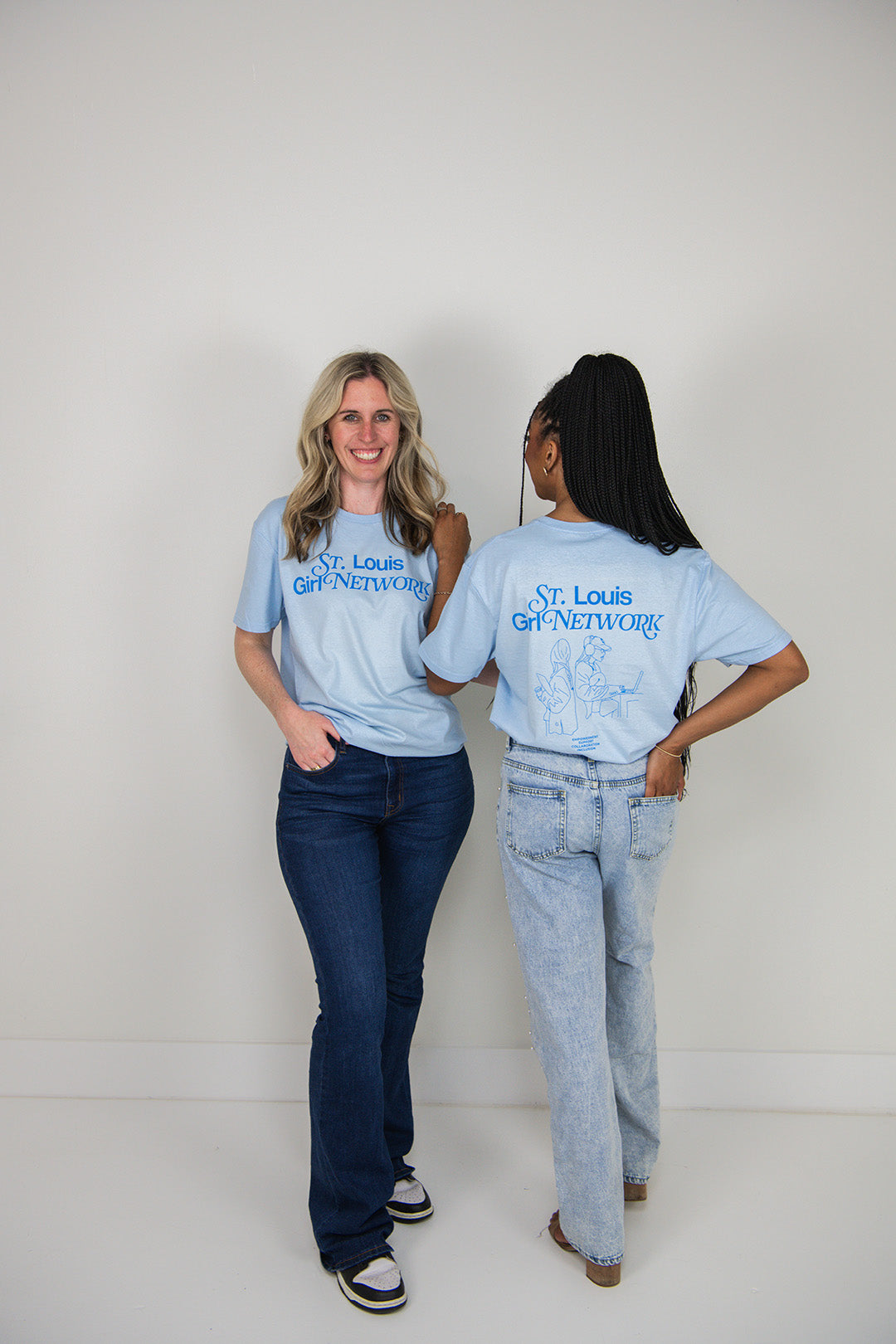 Two women wearing matching blue t-shirts with 'St. Louis Girl Network' text, standing side by side against a white background.