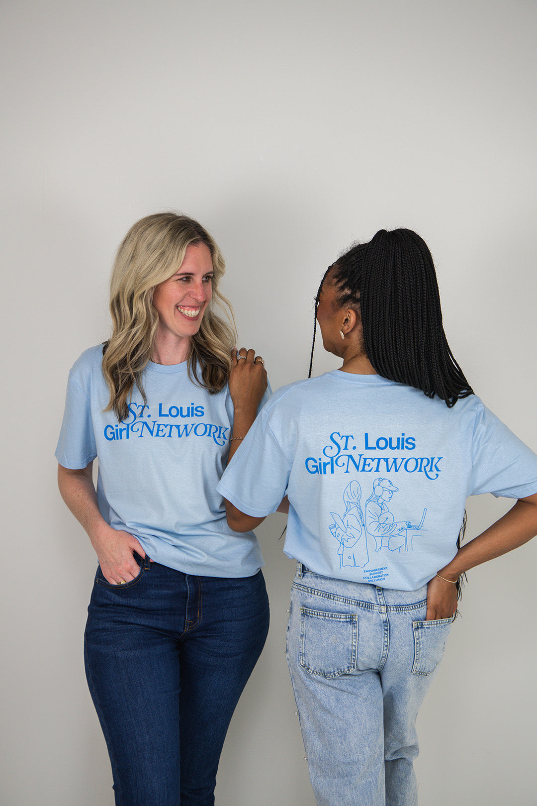 Two people wearing light blue t-shirts with 'St. Louis Girl Network' text, one facing the camera and the other showing the back.
