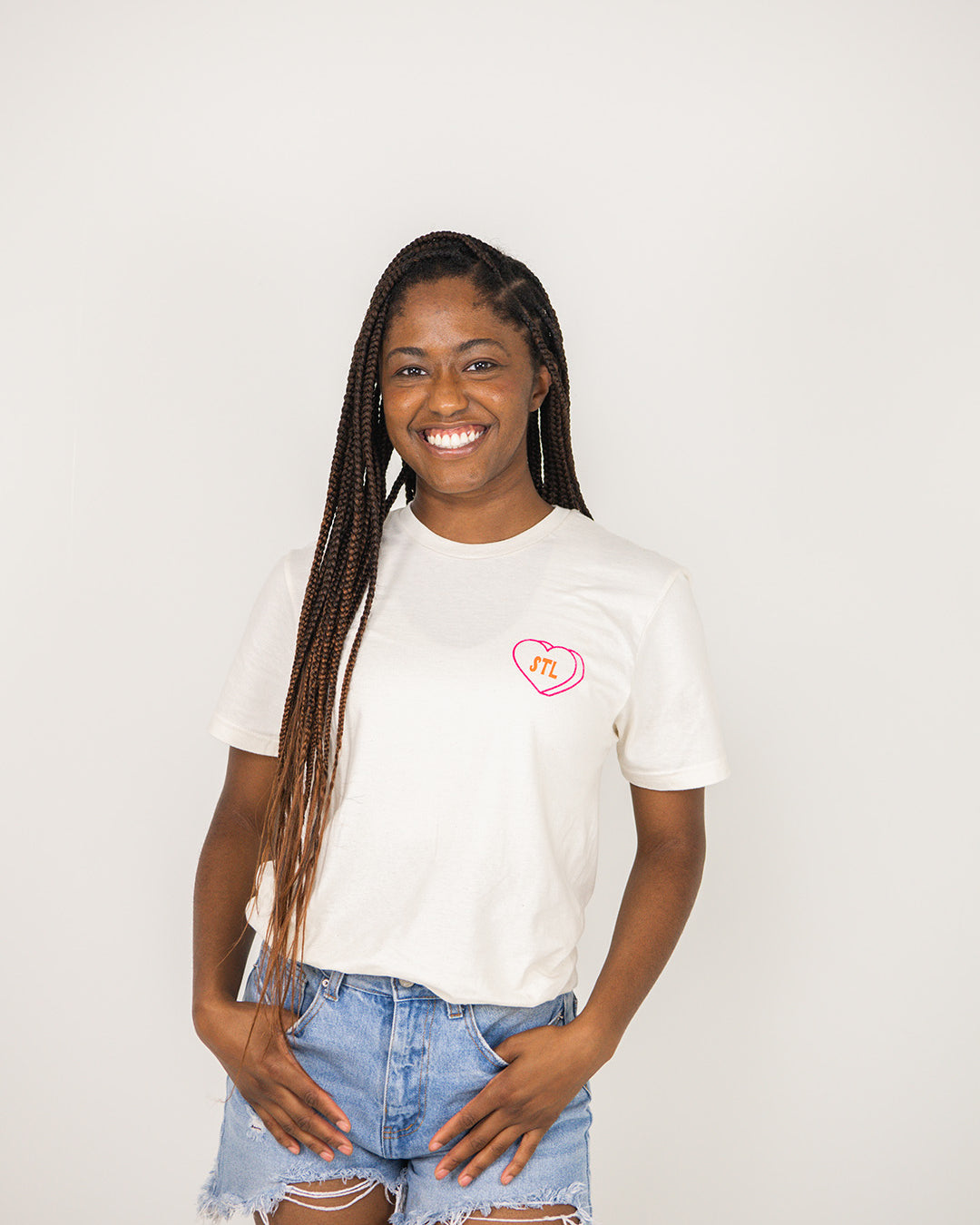 Woman wearing a beige t-shirt with a STL heart design on a plain background