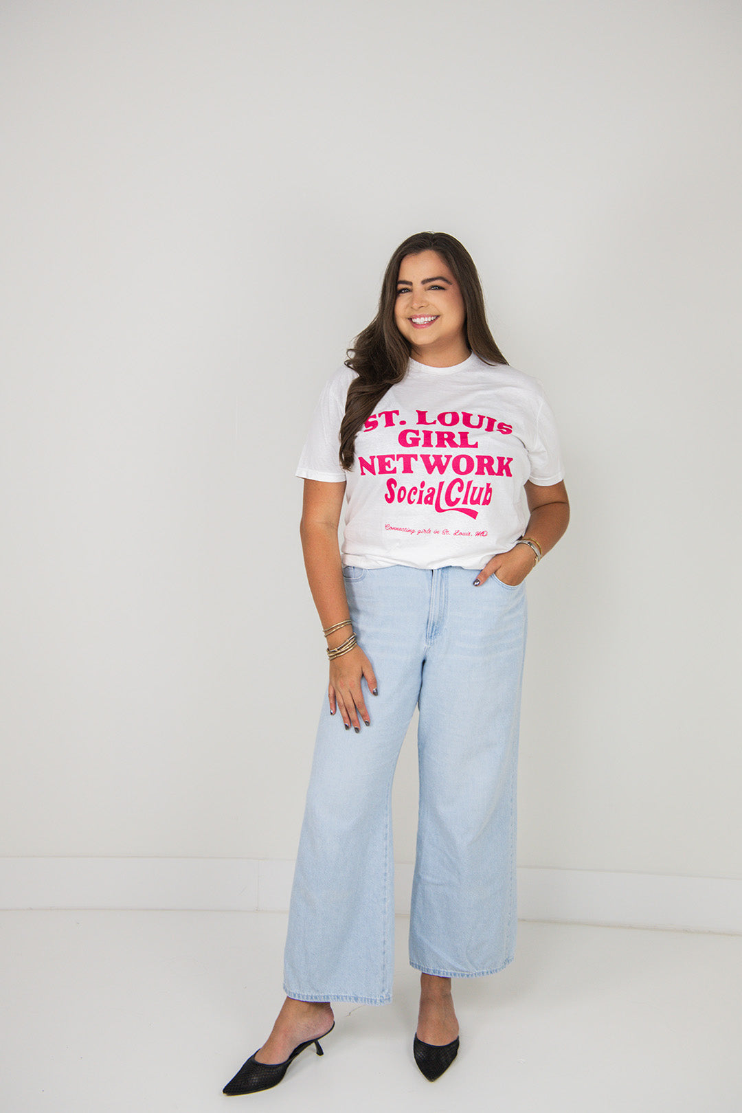 Woman wearing a white t-shirt with text and light blue jeans on a plain background