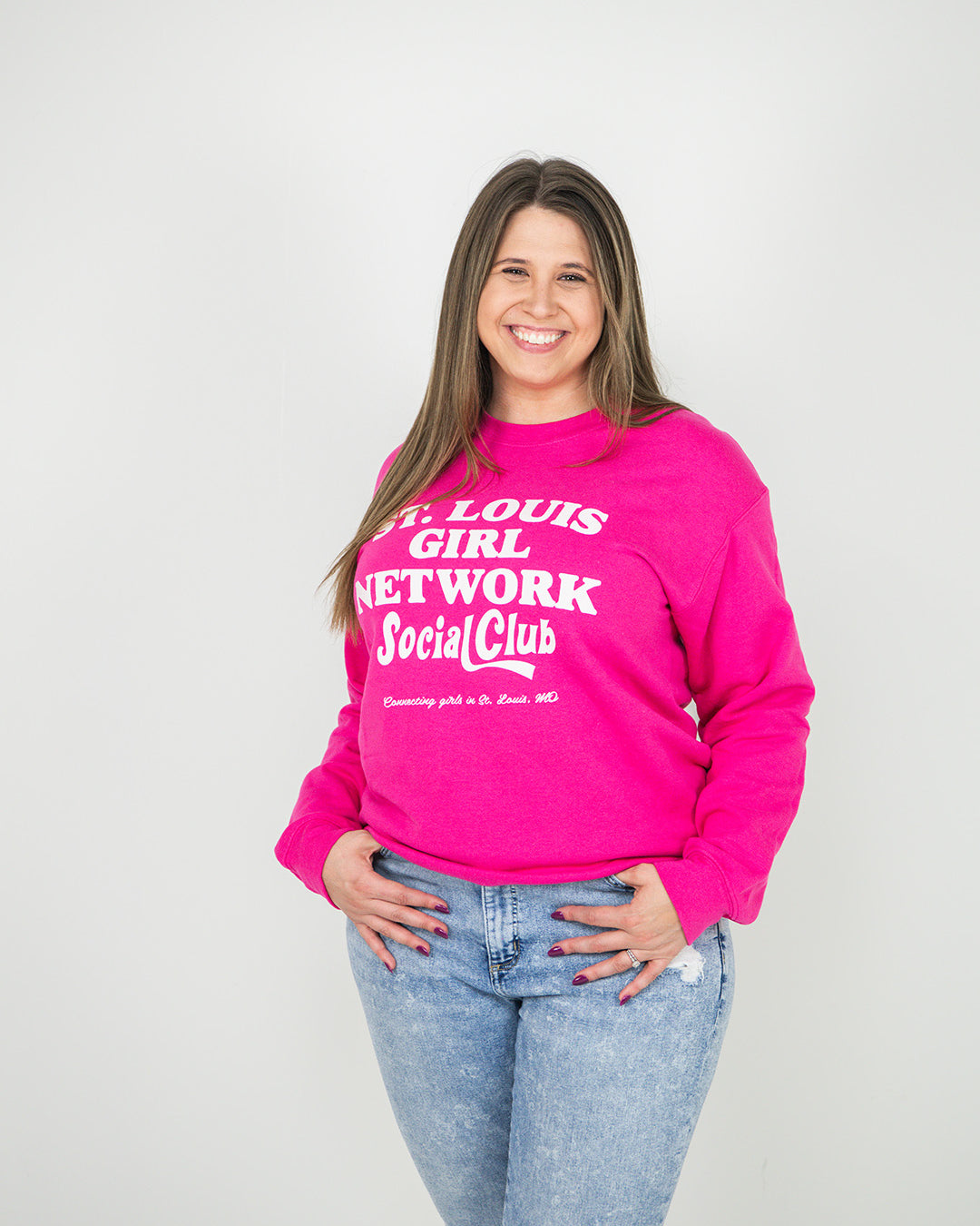 Woman wearing a pink sweatshirt with text, standing against a plain background