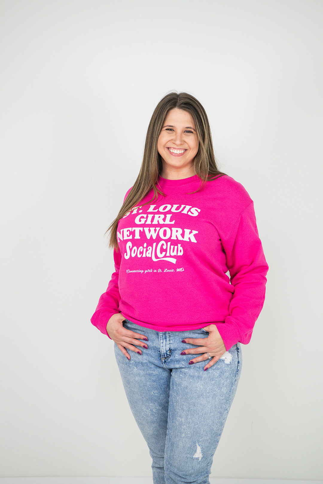 Woman wearing a pink sweatshirt with text, standing against a plain background