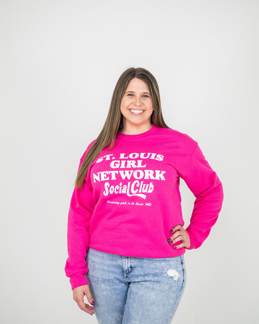 Person wearing a pink sweatshirt with text, standing against a plain background