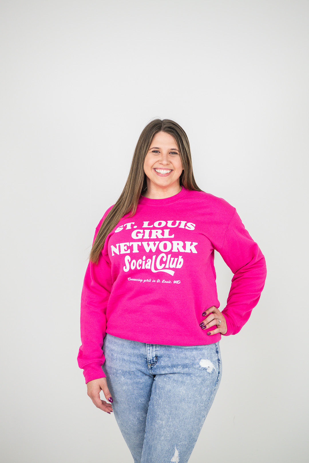 Person wearing a pink sweatshirt with text, standing against a plain background