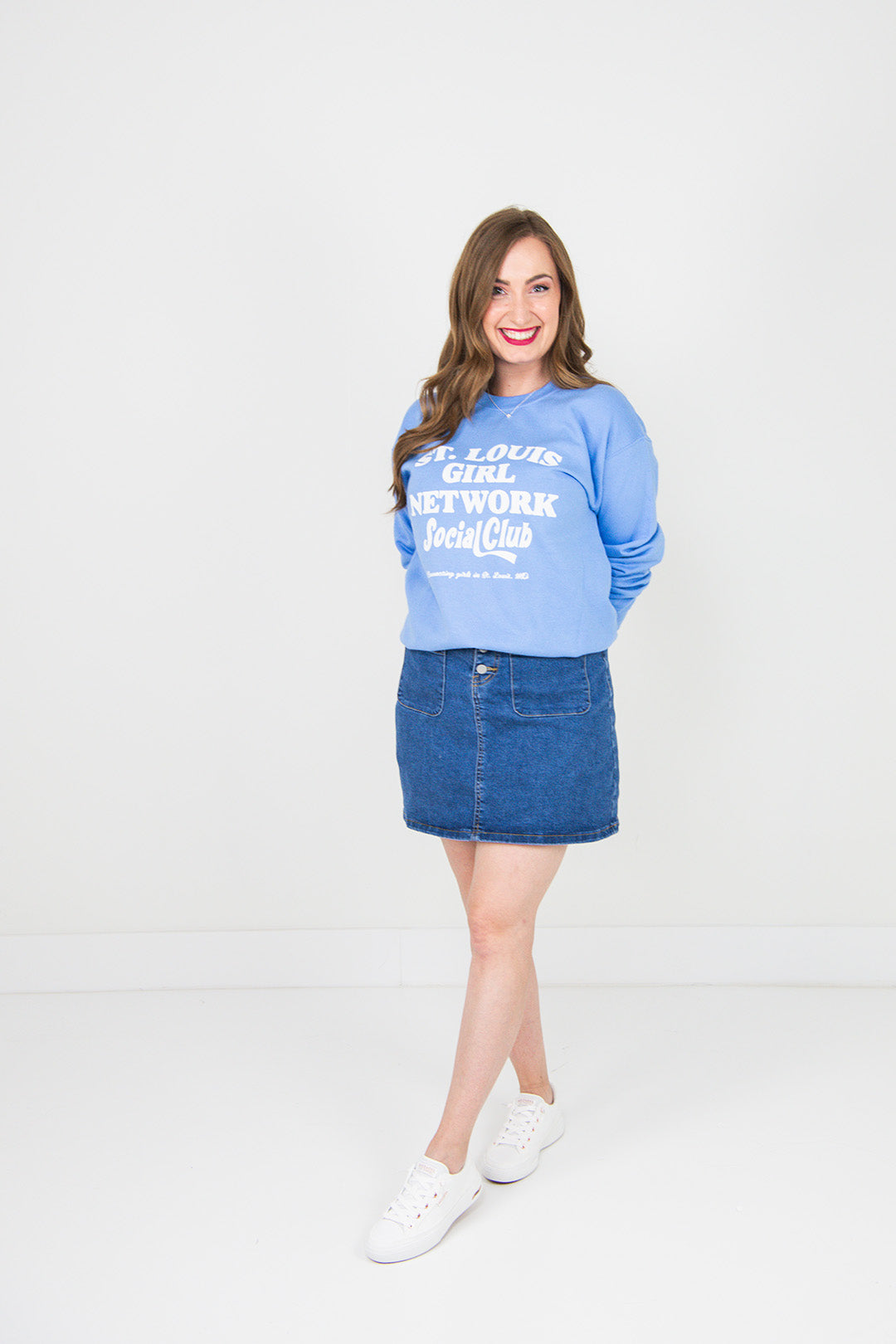 Woman wearing a blue sweatshirt and denim skirt on a white background