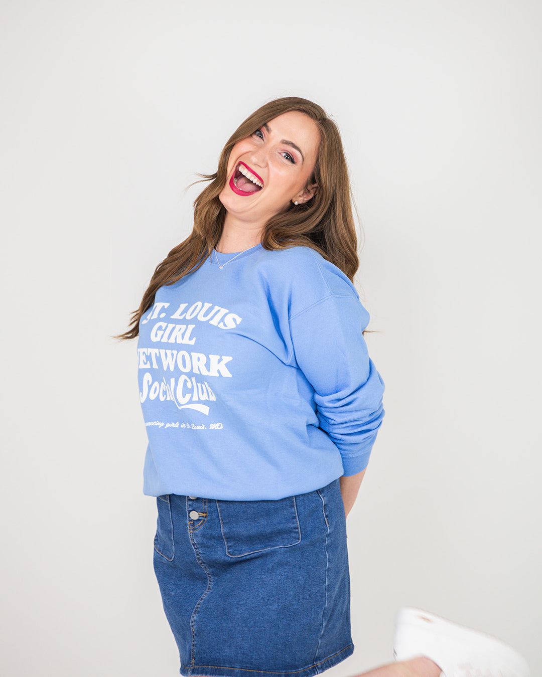 Woman wearing a blue sweatshirt with text and denim skirt on a white background