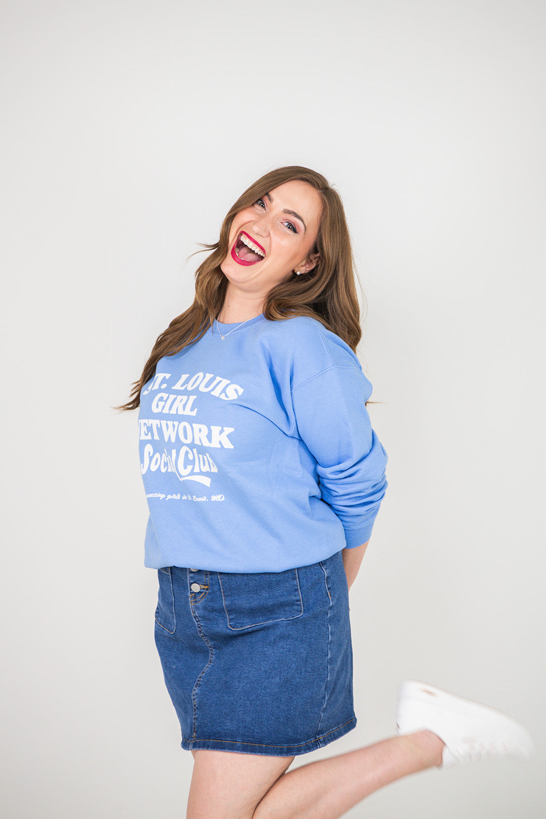 Woman wearing a blue sweatshirt with text and denim skirt on a white background