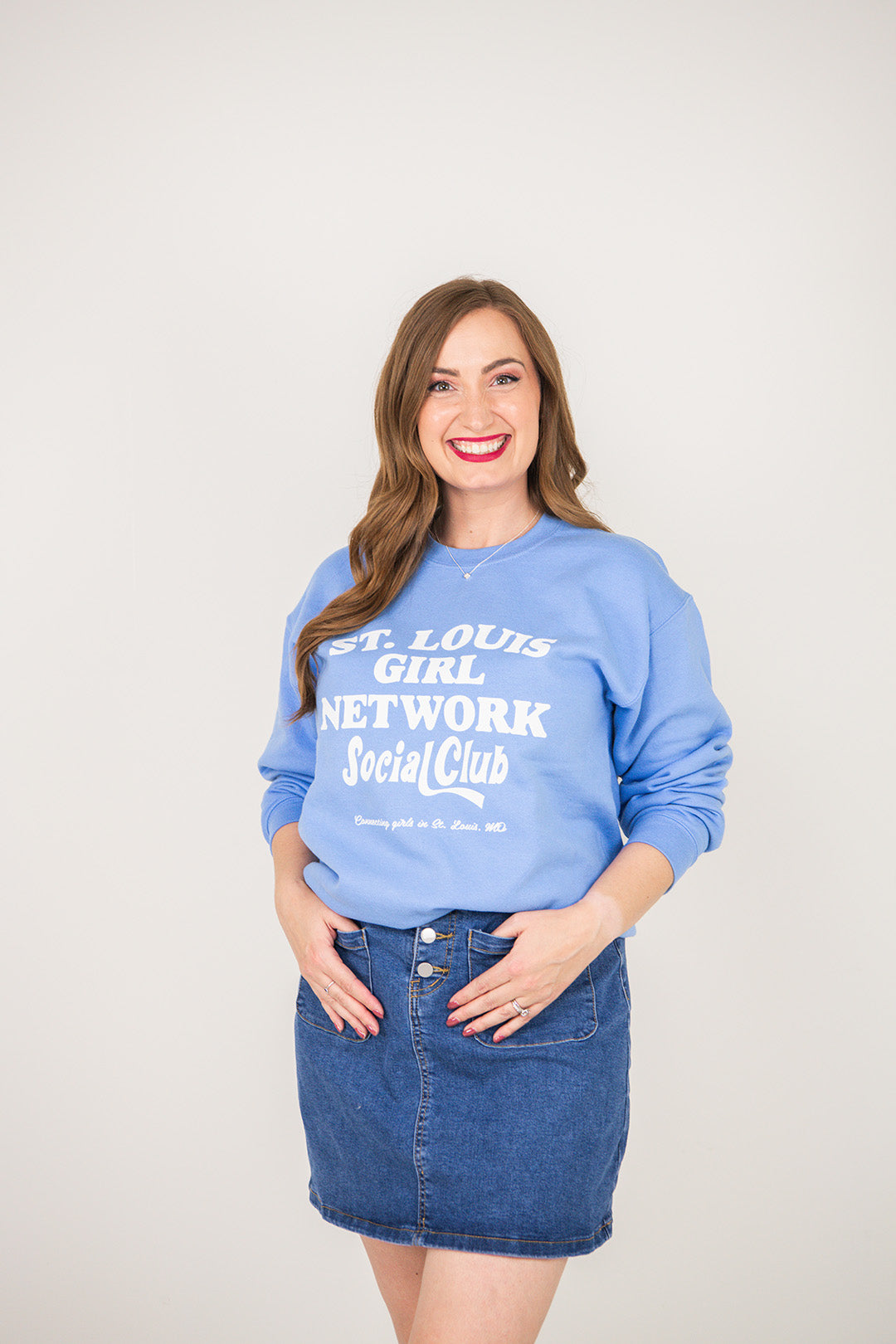 Woman wearing a blue sweatshirt with text, standing against a plain background
