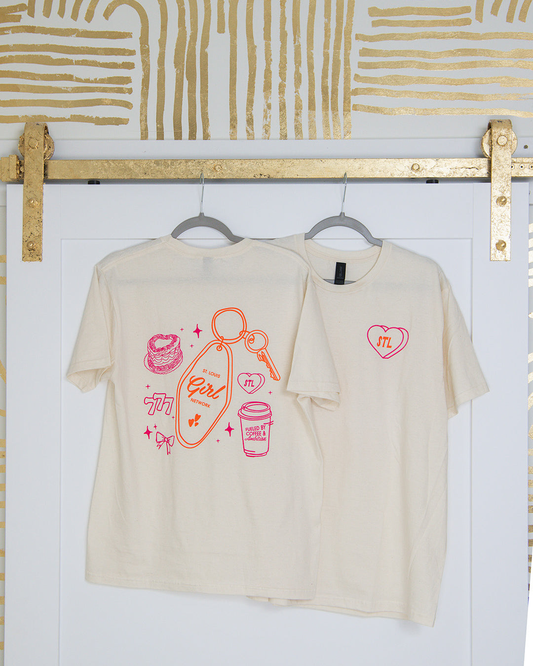 Beige t-shirt with graphic designs on a white wall with gold abstract patterns