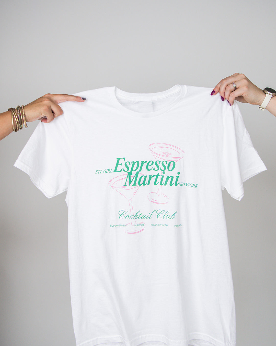 White t-shirt with 'Espresso Martini Cocktail Club' text held by two hands on a gray background