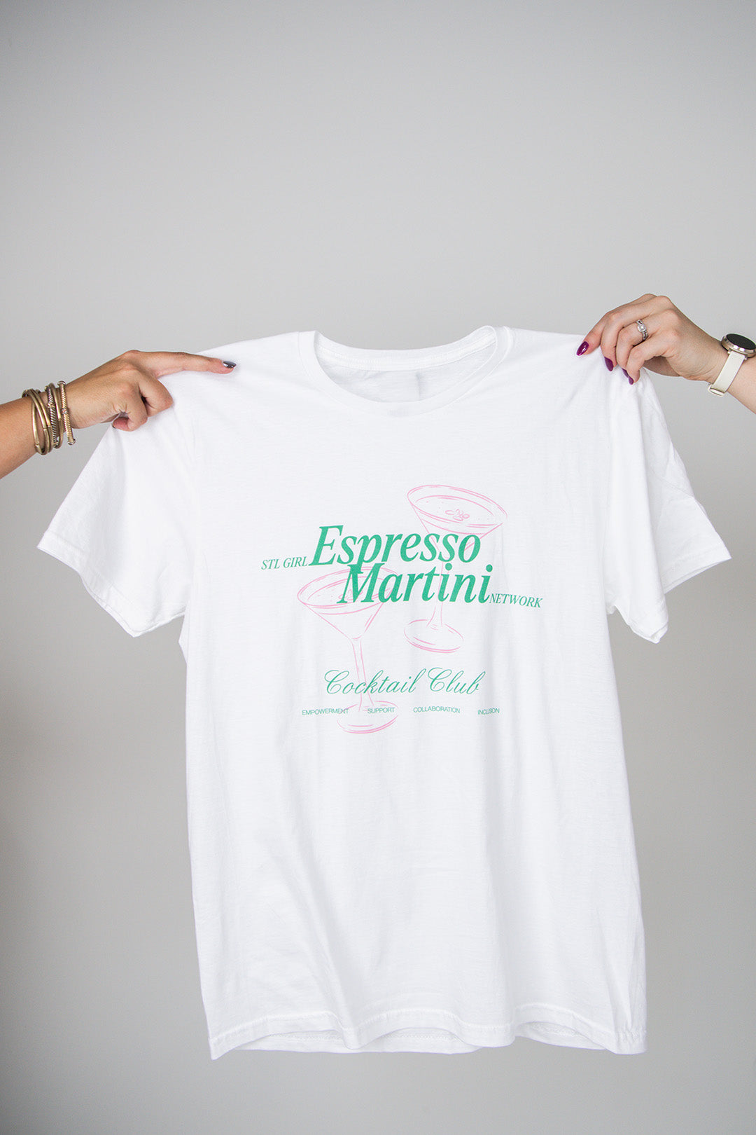 White t-shirt with 'Espresso Martini Cocktail Club' text held by two hands on a gray background