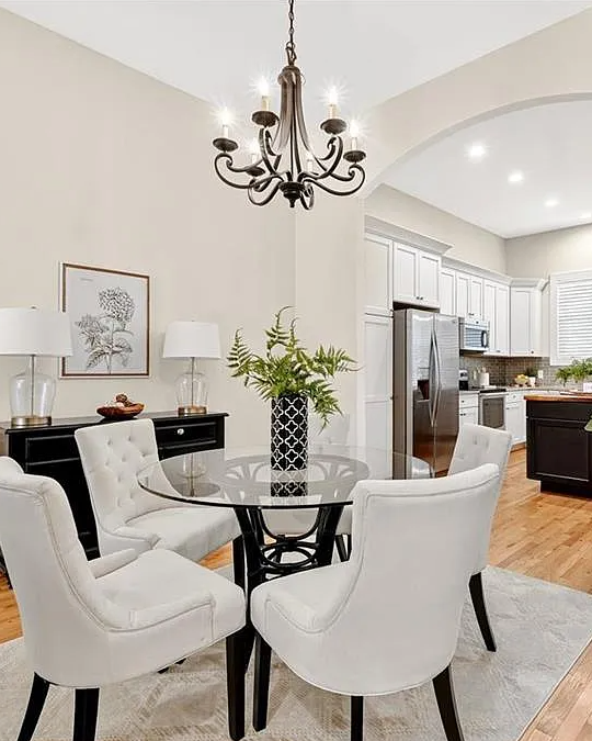 Modern dining room with white chairs, glass table, and kitchen in the background.