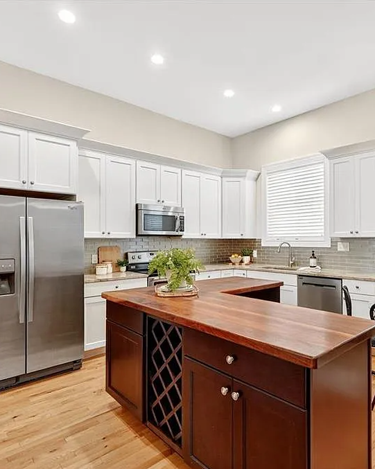 Modern kitchen with wooden island, stainless steel appliances, and white cabinets.