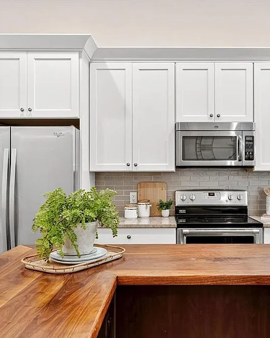 Modern kitchen with wooden island, stainless steel appliances, and white cabinets.