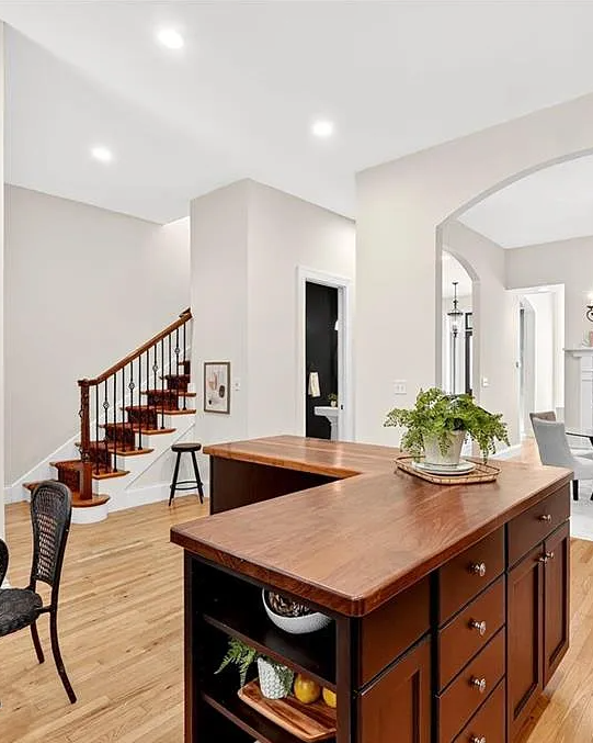 Modern home interior with wooden kitchen island, chairs, and staircase.