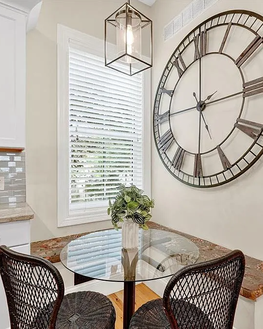 Kitchen with a large wall clock, dining table, and chairs.