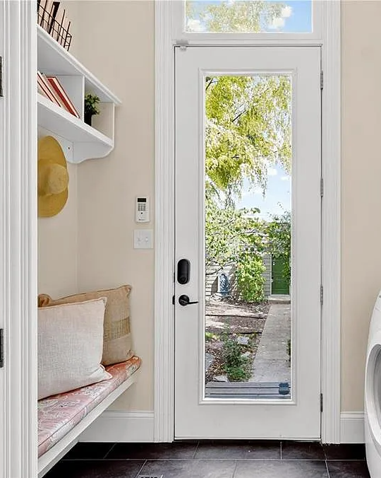 Laundry room with a bench, washer, dryer, and a glass door leading outside.
