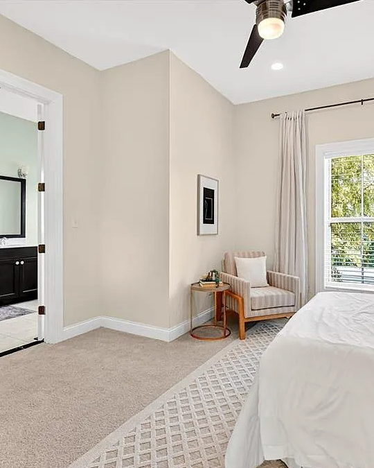Neatly arranged bedroom with a bed, chair, and bathroom in the background.
