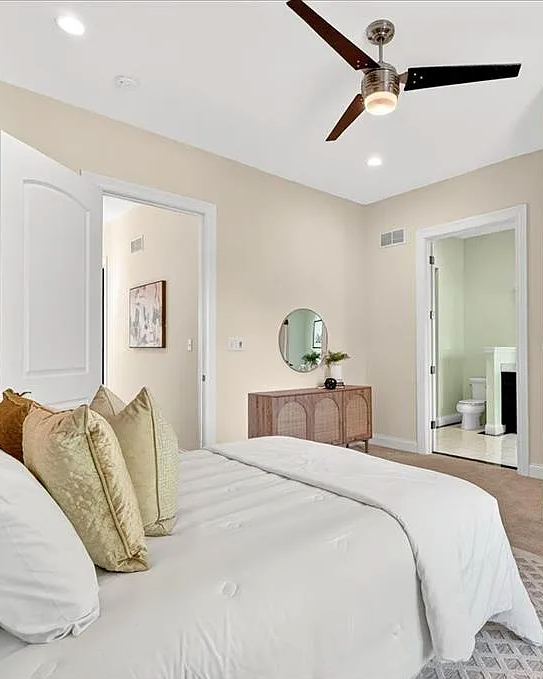 Neatly made bed in a bedroom with a mirror, lamp, and chair.