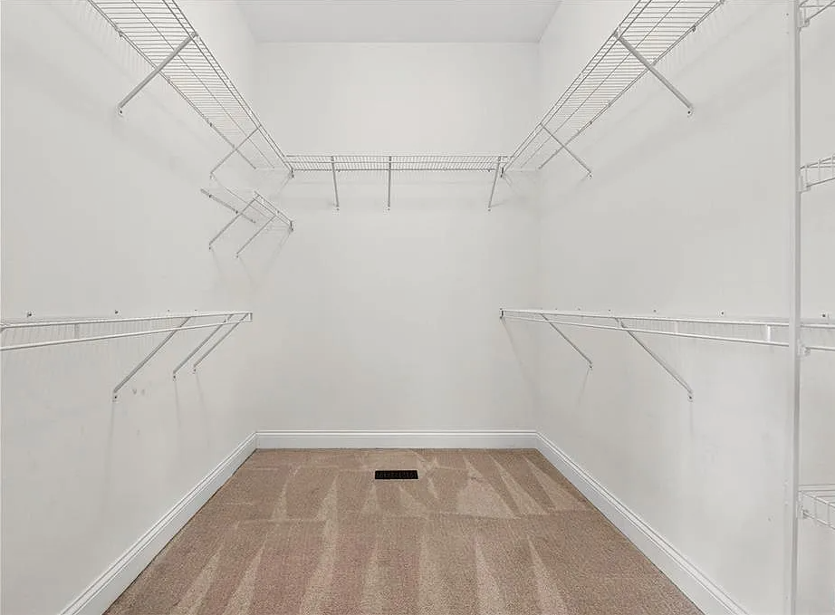 Empty closet with white walls, wooden floor, and metal rods.