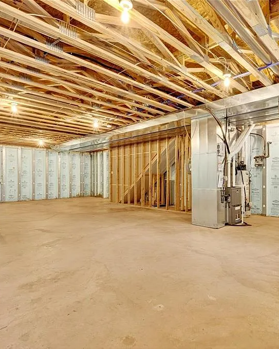 Basement with unfinished wooden ceiling and floor, exposed pipes, and concrete walls.