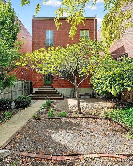 Backyard with garden bed, steps leading to a house, and trees on a sunny day.