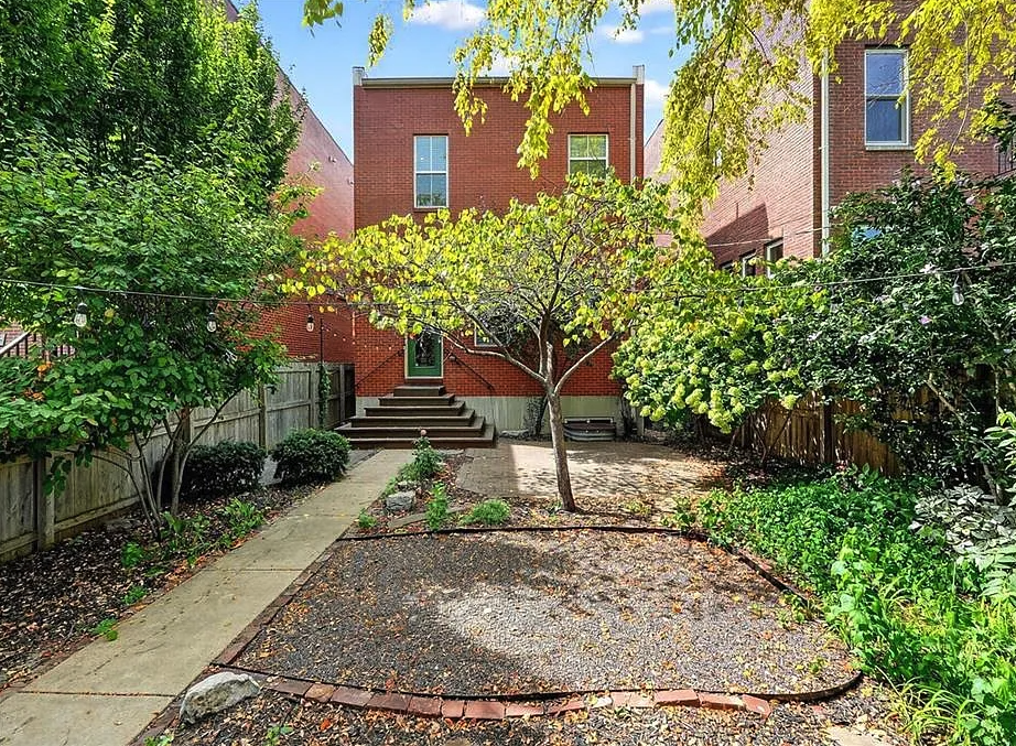 Backyard with garden bed, steps leading to a house, and trees on a sunny day.