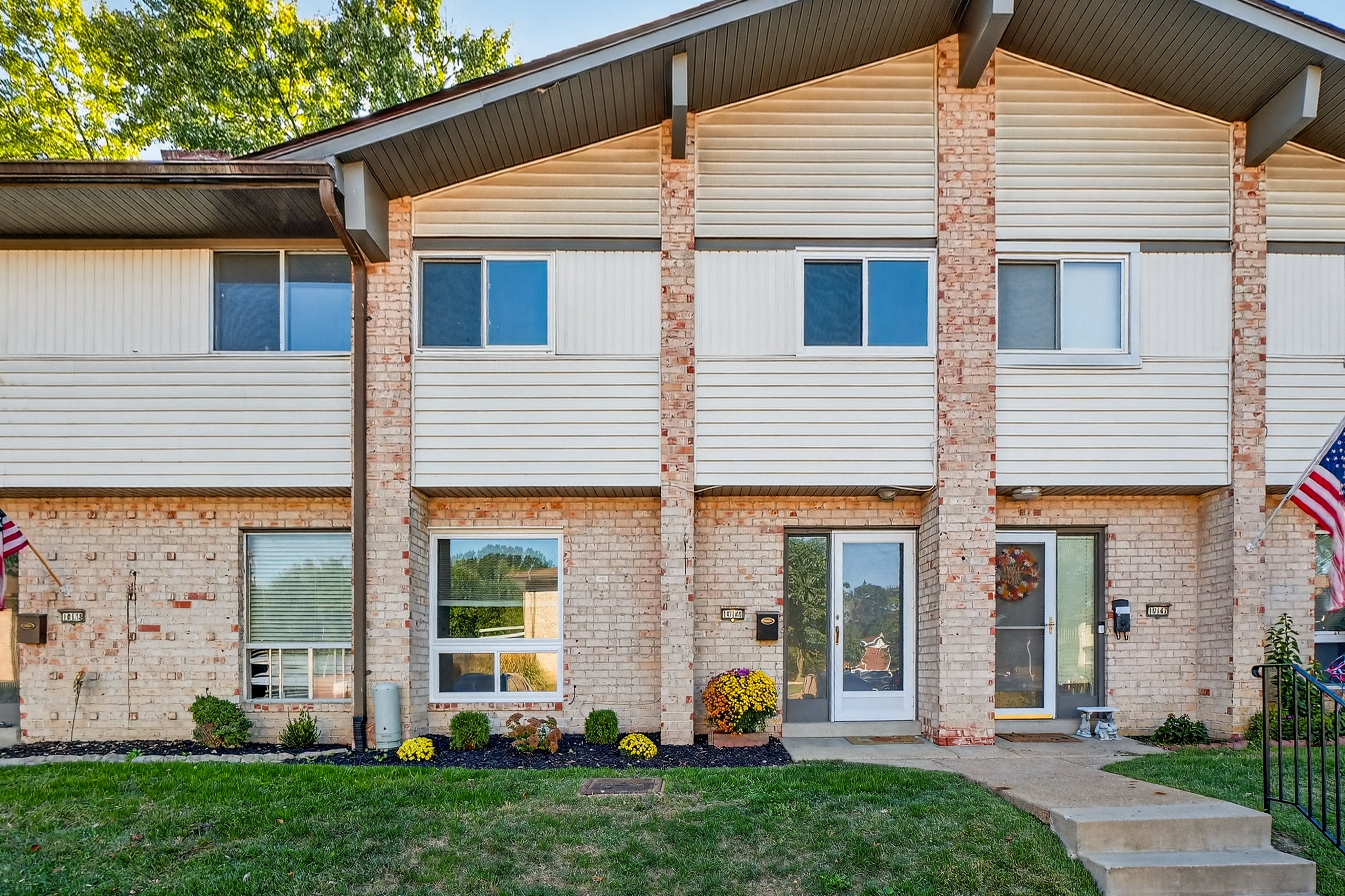 Two-story condo with brick and siding exterior, front yard, and American flag.