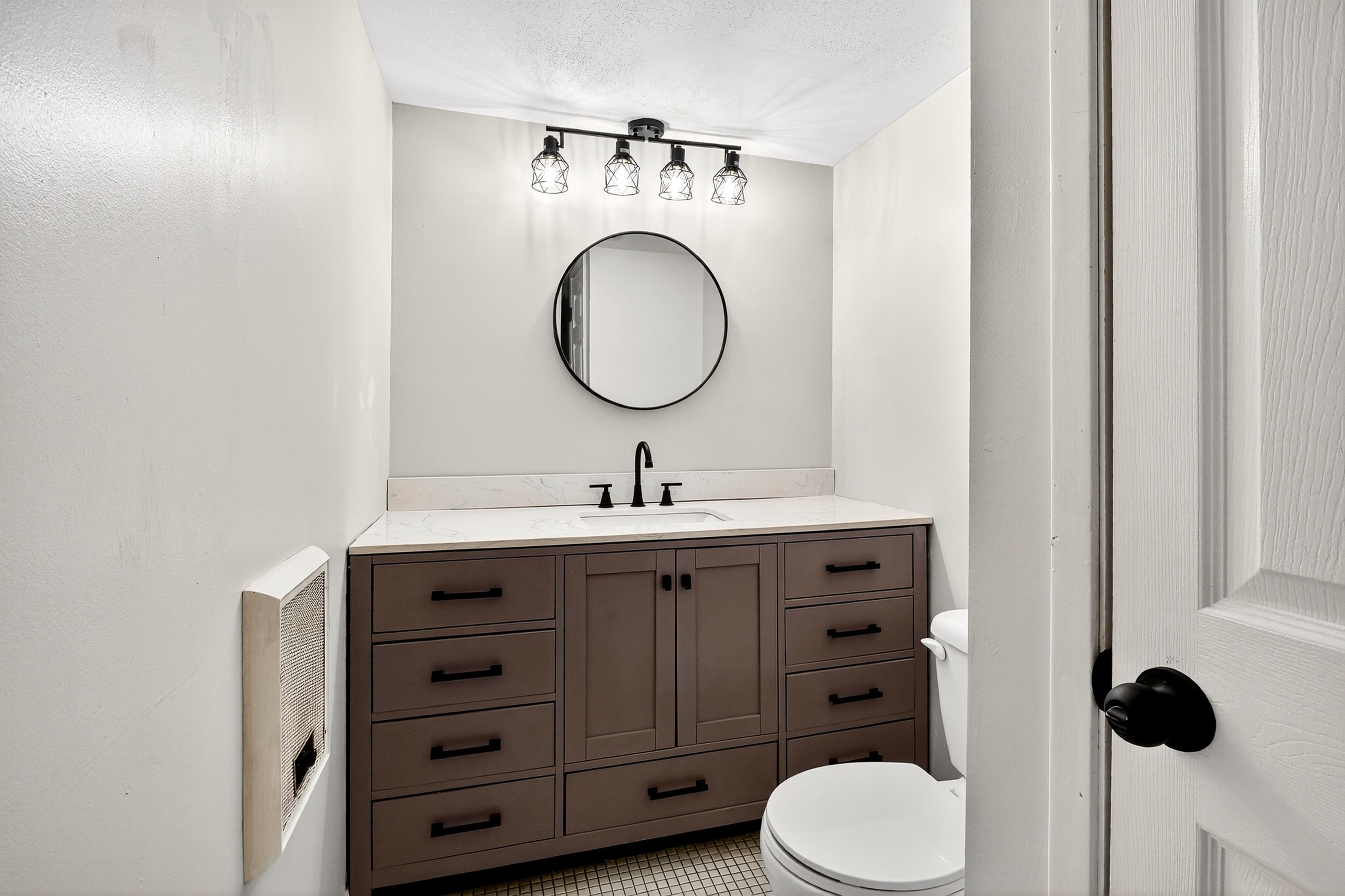 Bathroom with wooden vanity, round mirror, and toilet.
