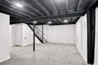 Basement with black ceiling beams, carpeted floor, and white walls.