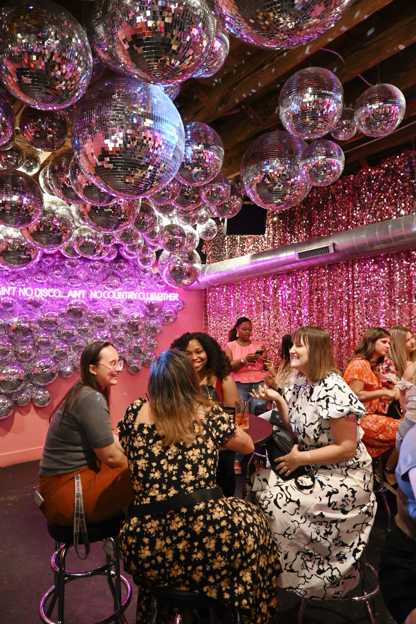 People socializing in a room with disco balls and pink walls