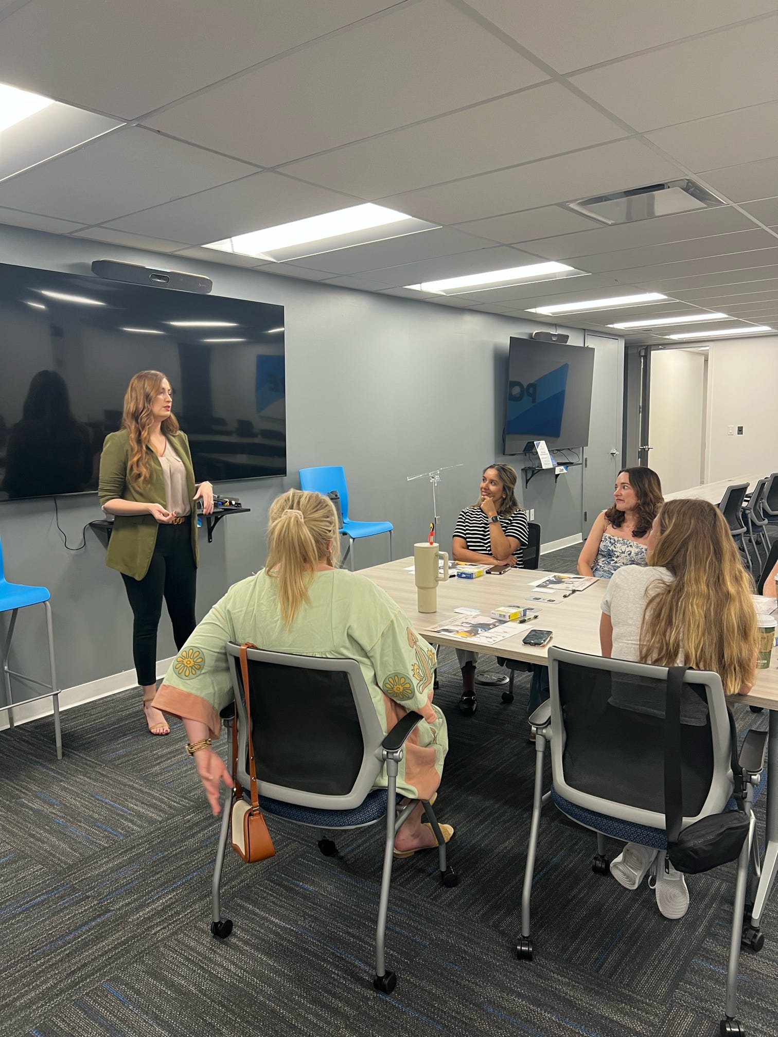 Group of people in a meeting room with one person standing and addressing the seated group.